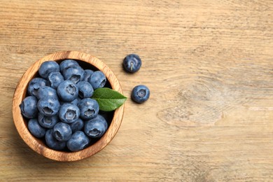 Bowl of fresh tasty blueberries on wooden table, flat lay. Space for text