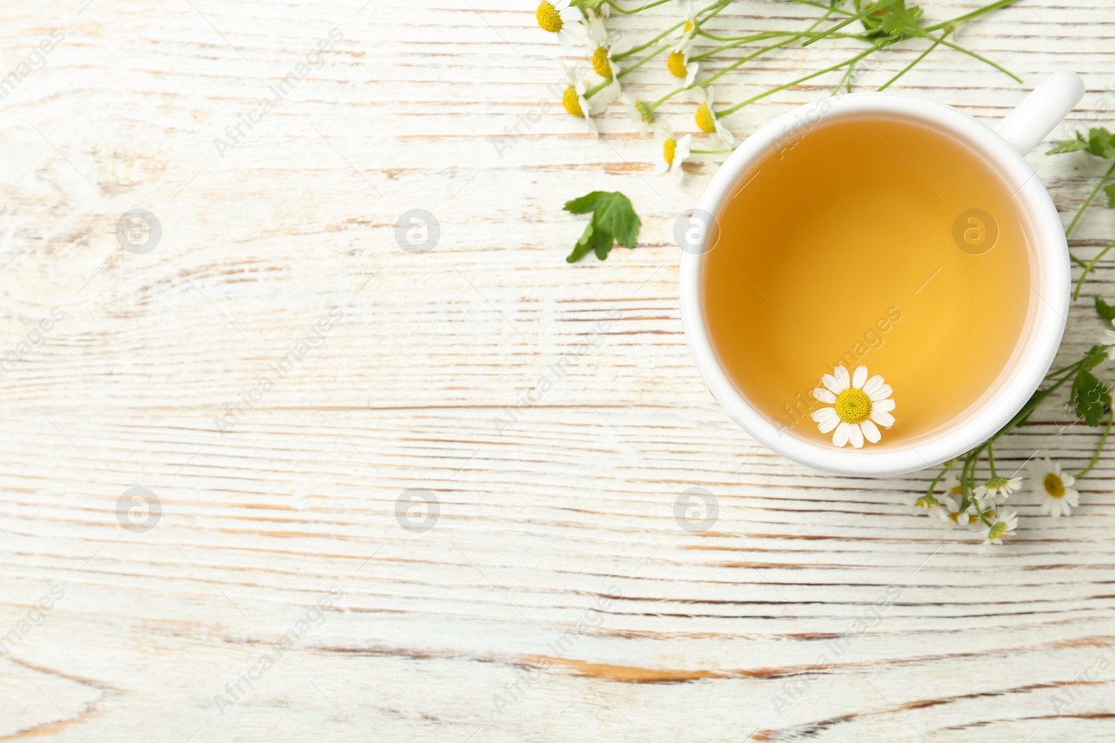 Photo of Cup of tea and chamomile flowers on white wooden table, flat lay. Space for text