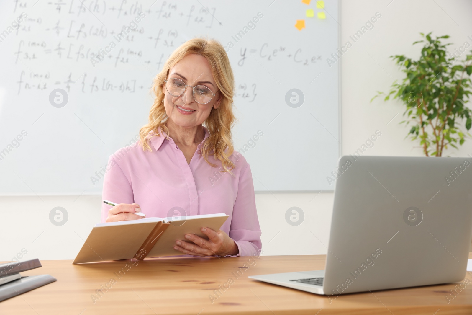 Photo of Teacher giving lesson near laptop at desk in classroom