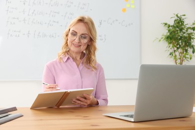 Teacher giving lesson near laptop at desk in classroom