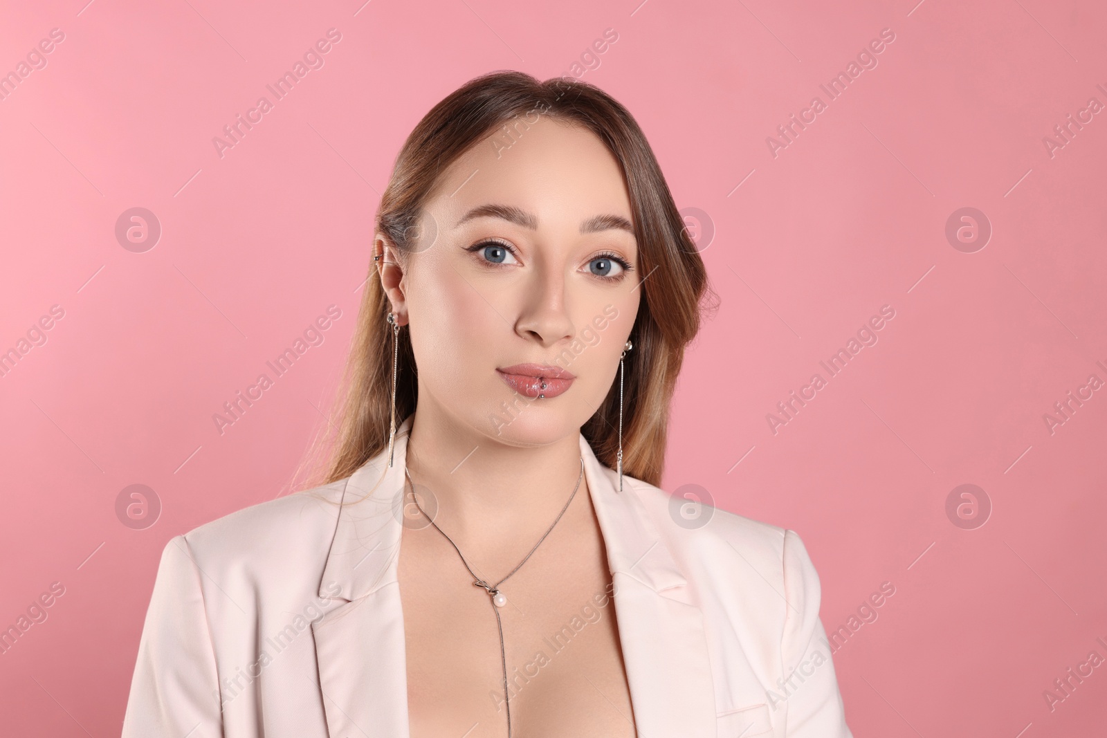 Photo of Young woman with lip and ear piercings on pink background