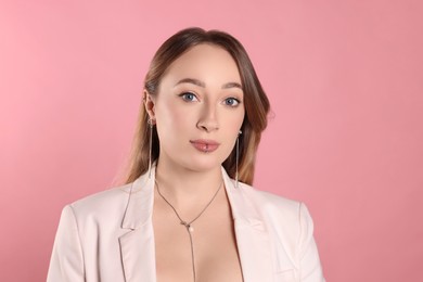 Photo of Young woman with lip and ear piercings on pink background