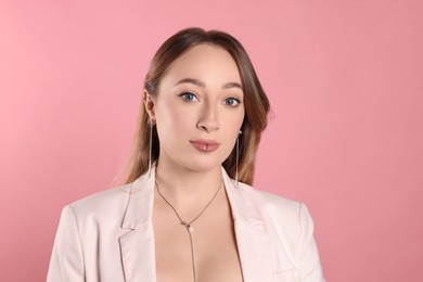 Young woman with lip and ear piercings on pink background