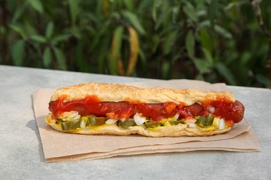 Photo of Fresh tasty hot dog with ketchup on light grey parapet outdoors