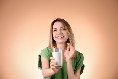 Beautiful young woman drinking milk on color background