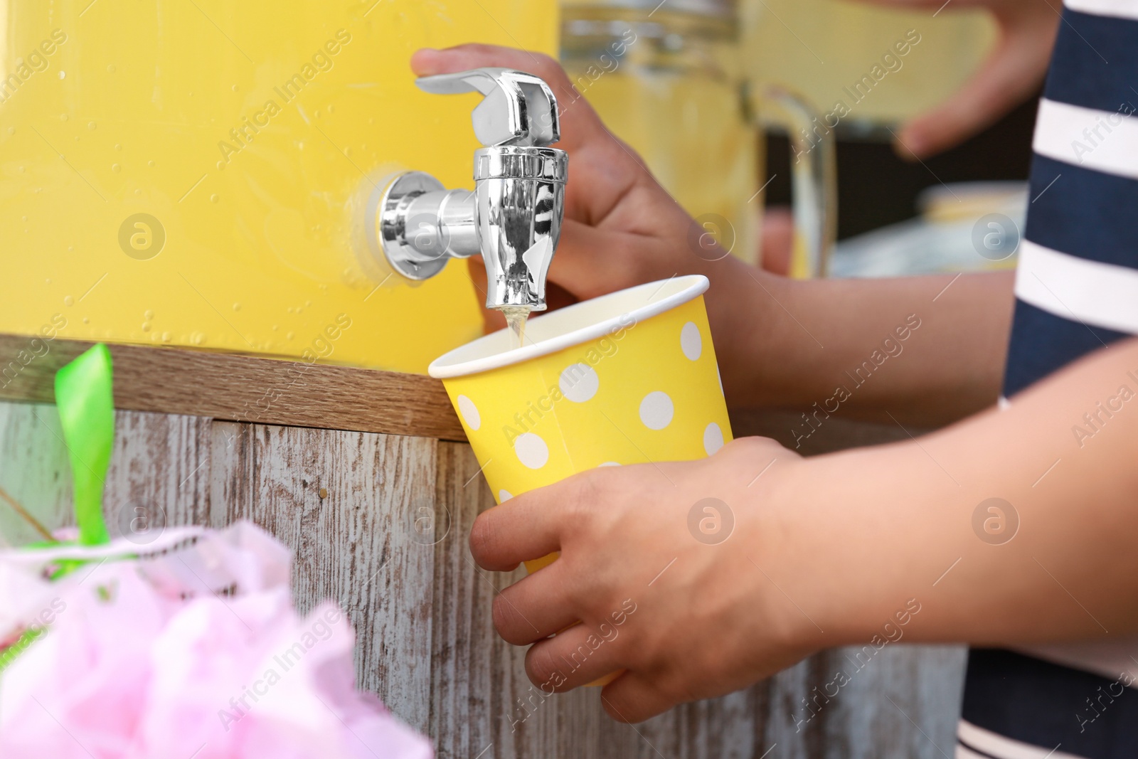 Photo of Little girl pouring natural lemonade into cup, closeup. Summer refreshing drink