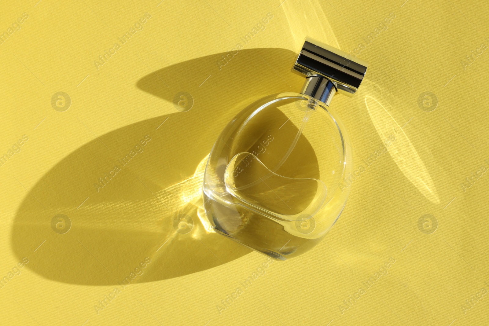 Photo of Luxury women's perfume. Sunlit glass bottle on yellow background, top view