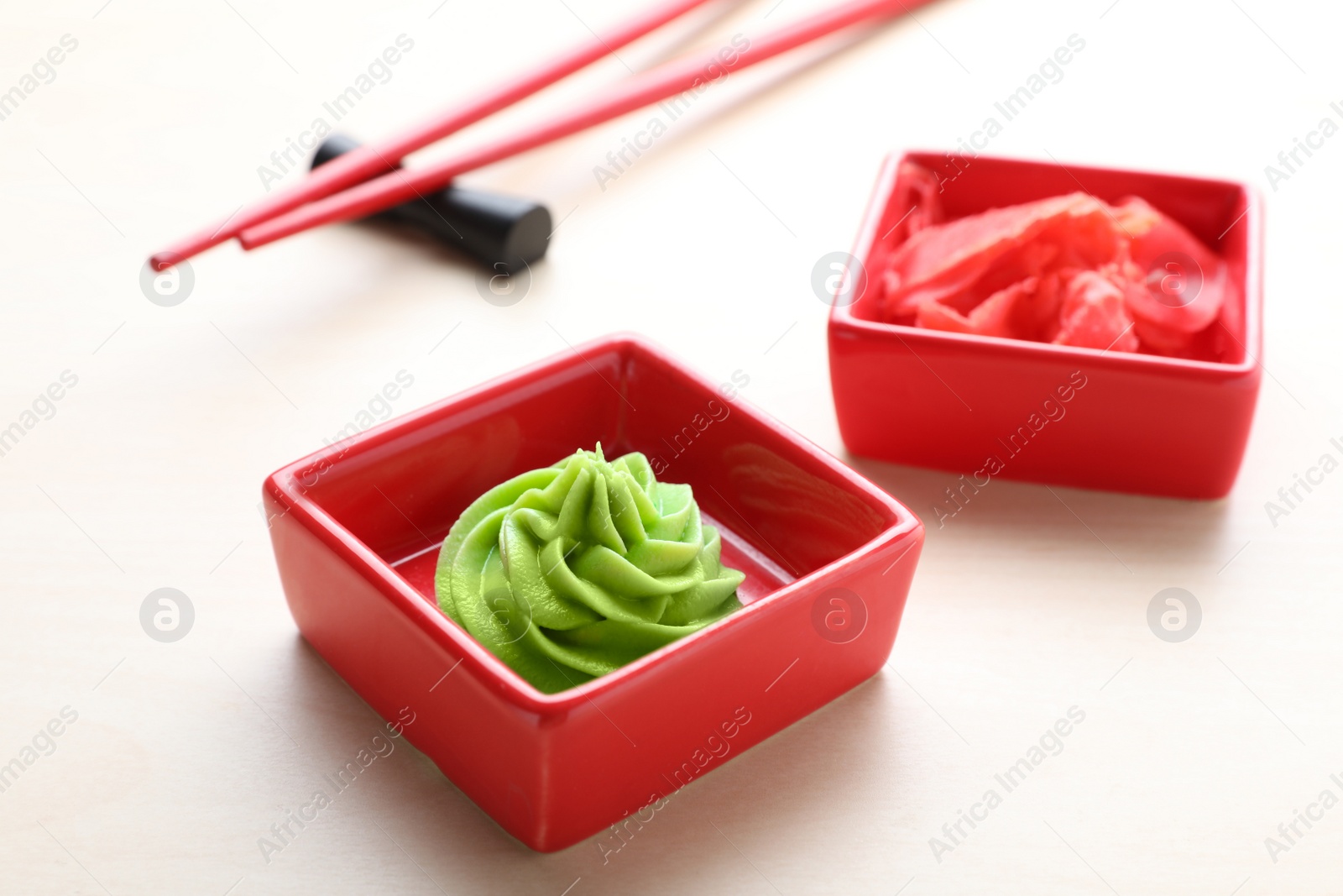 Photo of Bowls with swirl of wasabi paste and pickled ginger on white table, closeup