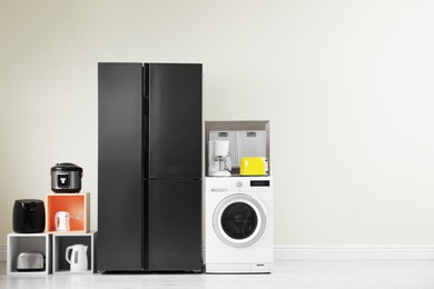 Modern refrigerator and other household appliances near beige wall indoors, space for text