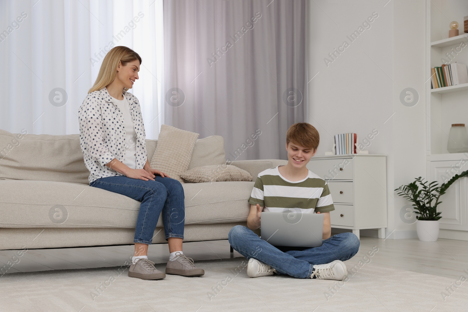 Photo of Happy mother and her teenage son spending time together with laptop on floor at home