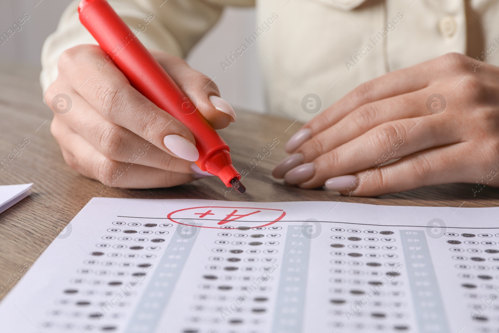 Photo of School grade. Teacher writing letter A with plus symbol on answer sheet at wooden table, closeup