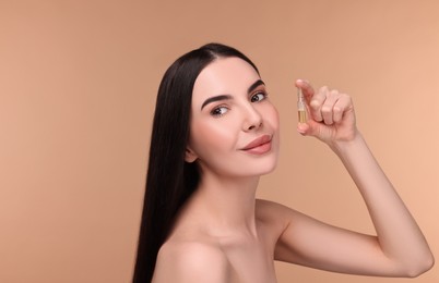 Photo of Beautiful young woman holding skincare ampoule on beige background. Space for text