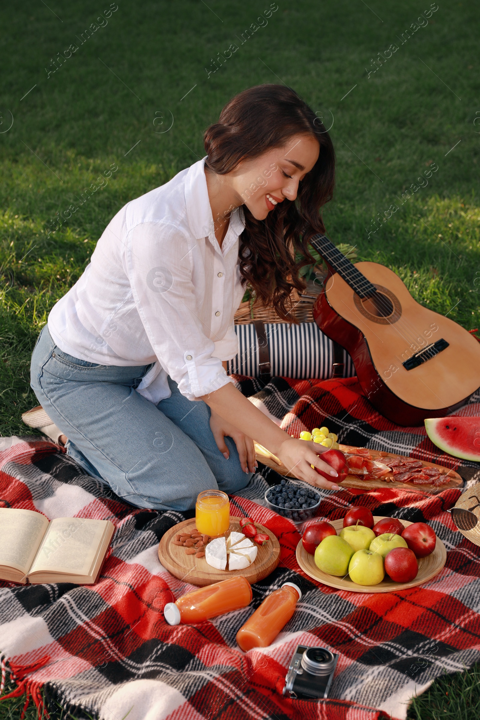 Photo of Happy young woman having picnic on plaid outdoors