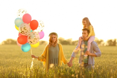 Photo of Happy family with colorful balloons in field on sunny day