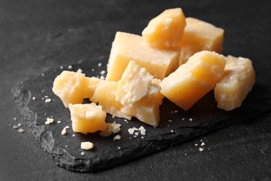 Photo of Pieces of delicious parmesan cheese on black table, closeup