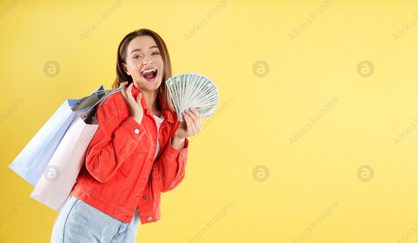 Photo of Emotional young woman with money and shopping bags on yellow background. Space for text