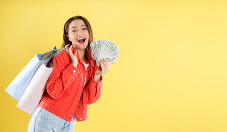 Emotional young woman with money and shopping bags on yellow background. Space for text