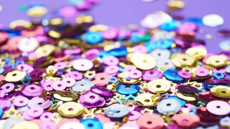 Many different colorful sequins on purple background, closeup