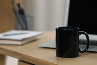 Photo of Black ceramic mug and laptop on wooden table at workplace. Space for text