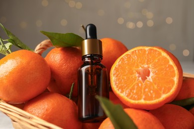 Photo of Bottle of tangerine essential oil and fresh fruits in basket, closeup