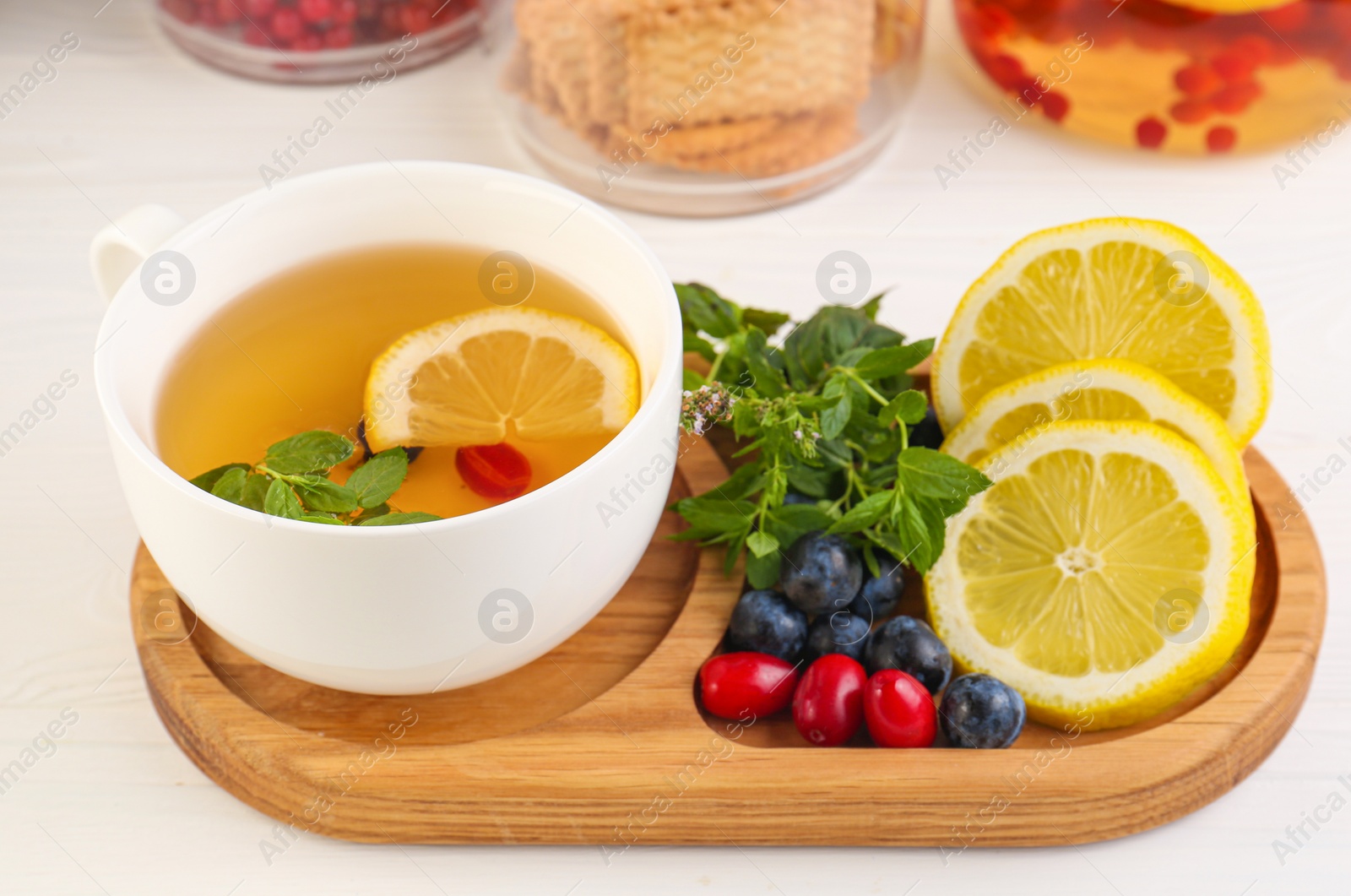 Photo of Cup with delicious immunity boosting tea and ingredients on white wooden table, closeup