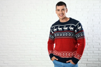 Portrait of young man in Christmas sweater near white brick wall. Space for text