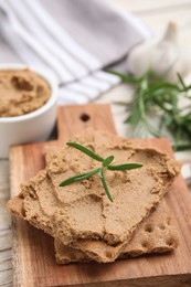 Photo of Crispy crackers with delicious meat pate and rosemary on wooden board, closeup