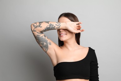 Beautiful woman with tattoos on arm against grey background