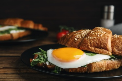 Photo of Delicious croissant with arugula and fried egg on wooden table, closeup
