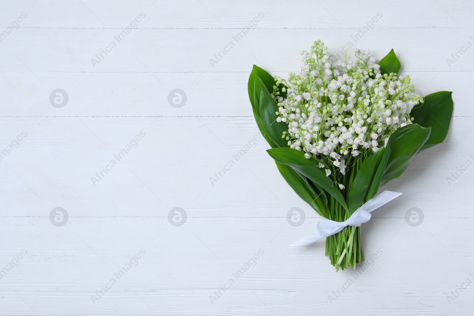 Photo of Beautiful lily of the valley flowers on white wooden table, top view. Space for text