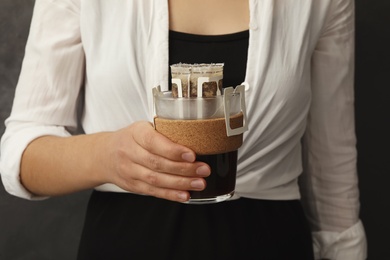 Photo of Woman holding cup with drip coffee bag on grey background, closeup