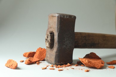 Photo of One sledgehammer and pieces of broken brick on grey background, closeup