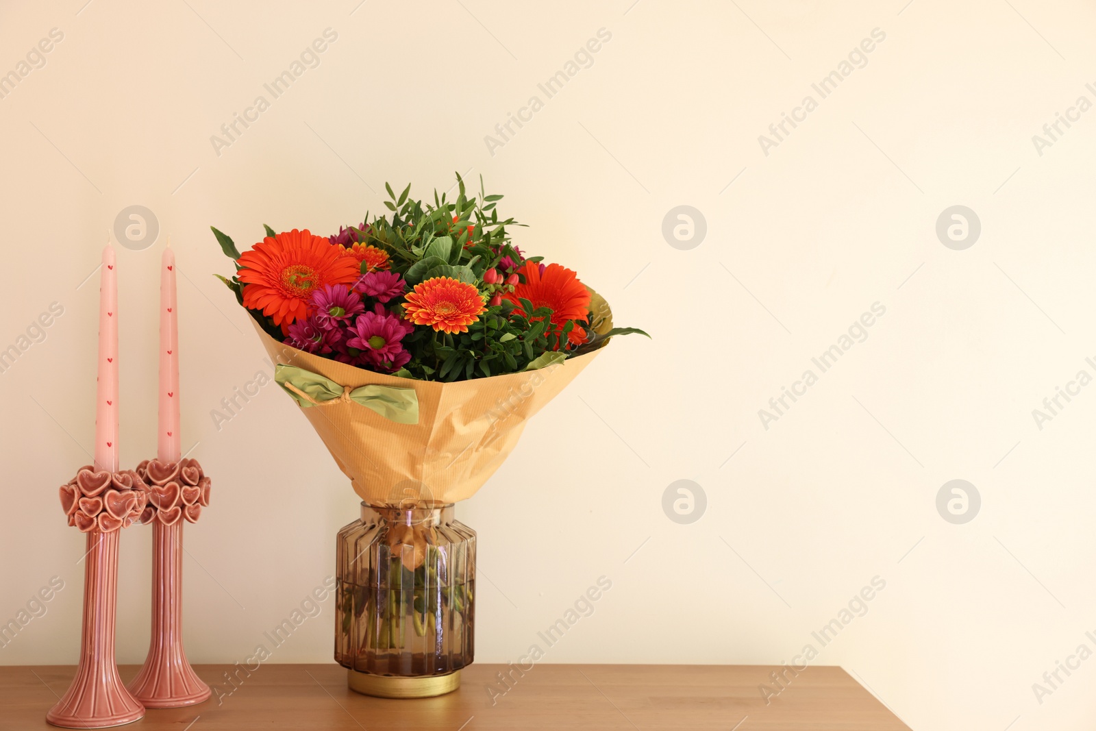 Photo of Bouquet of flowers and candles on wooden table near white wall. Space for text