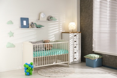 Cute nursery interior with comfortable crib near white wall