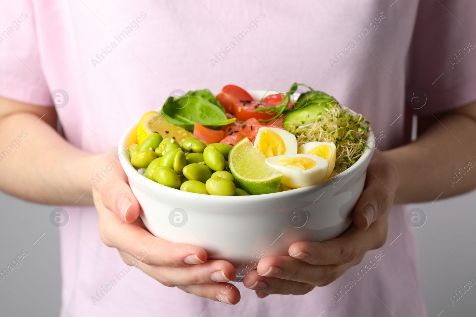 Photo of Woman holding delicious poke bowl quail eggs, fish and edamame beans on white background, closeup