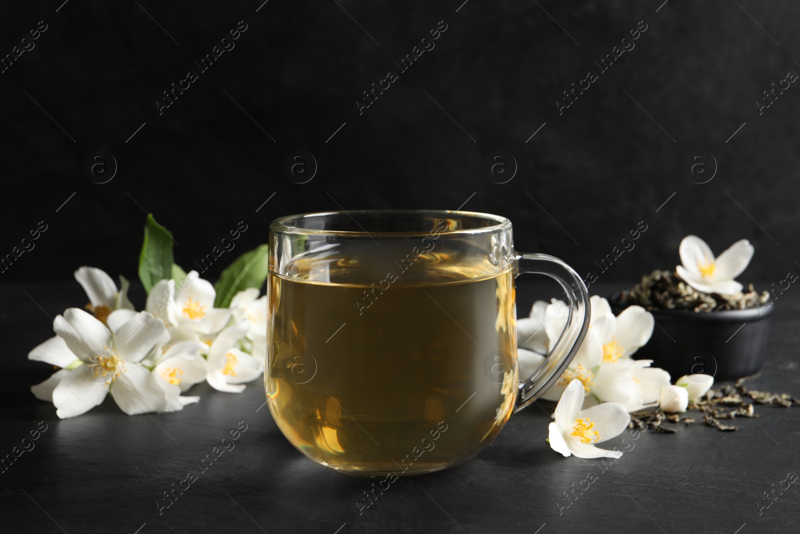 Photo of Glass cup of jasmine tea and fresh flowers on black table