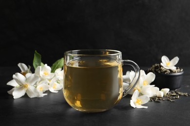 Glass cup of jasmine tea and fresh flowers on black table