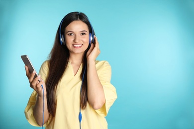Attractive woman with mobile phone enjoying music in headphones on color background. Space for text