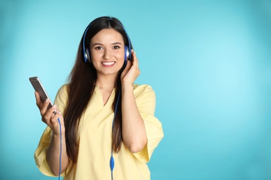 Photo of Attractive woman with mobile phone enjoying music in headphones on color background. Space for text