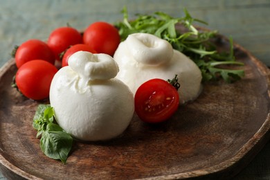Delicious burrata cheese with tomatoes and arugula on table, closeup