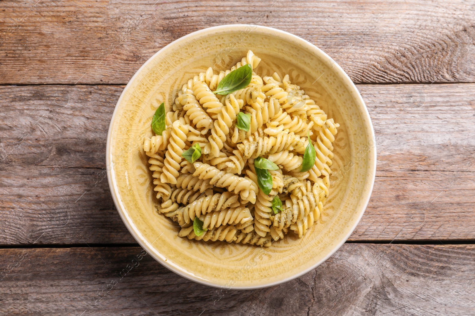 Photo of Plate of delicious basil pesto pasta on wooden background, top view