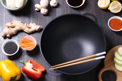 Photo of Empty iron wok, chopsticks and ingredients on dark grey wooden table, above view