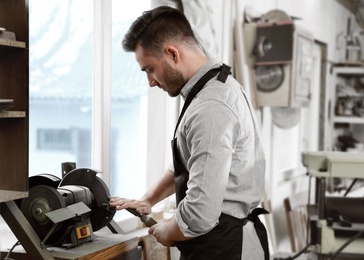 Photo of Young working man using grinding machine at carpentry shop