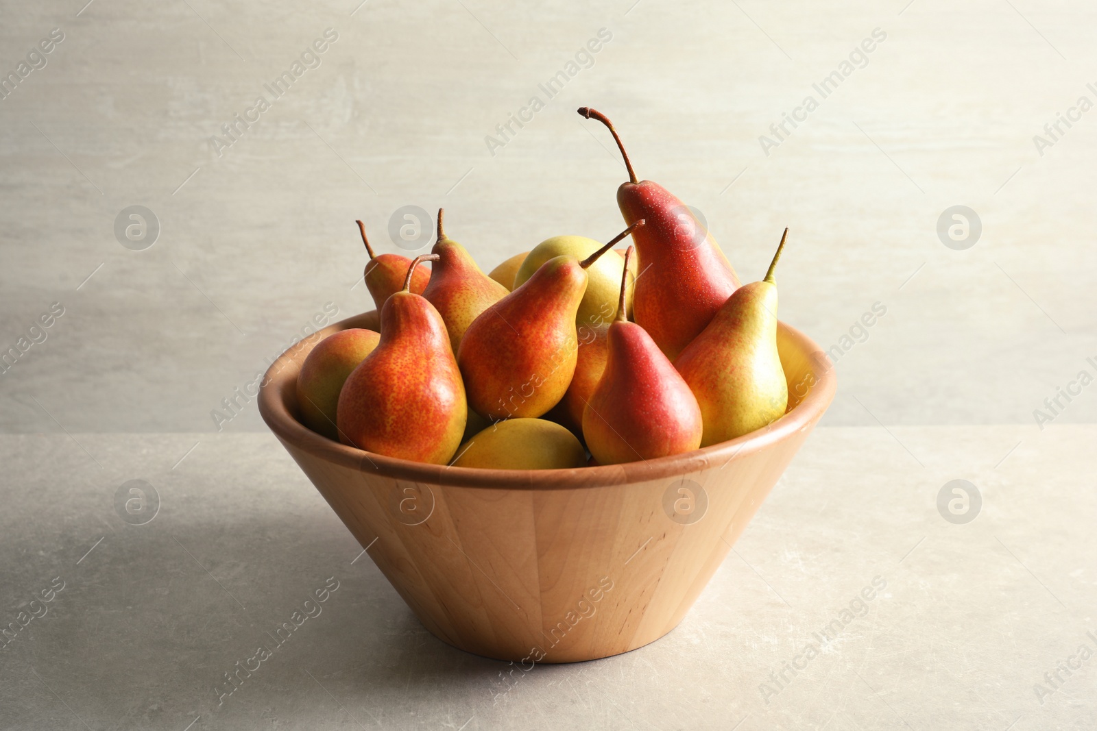 Photo of Bowl with ripe pears on table against light background