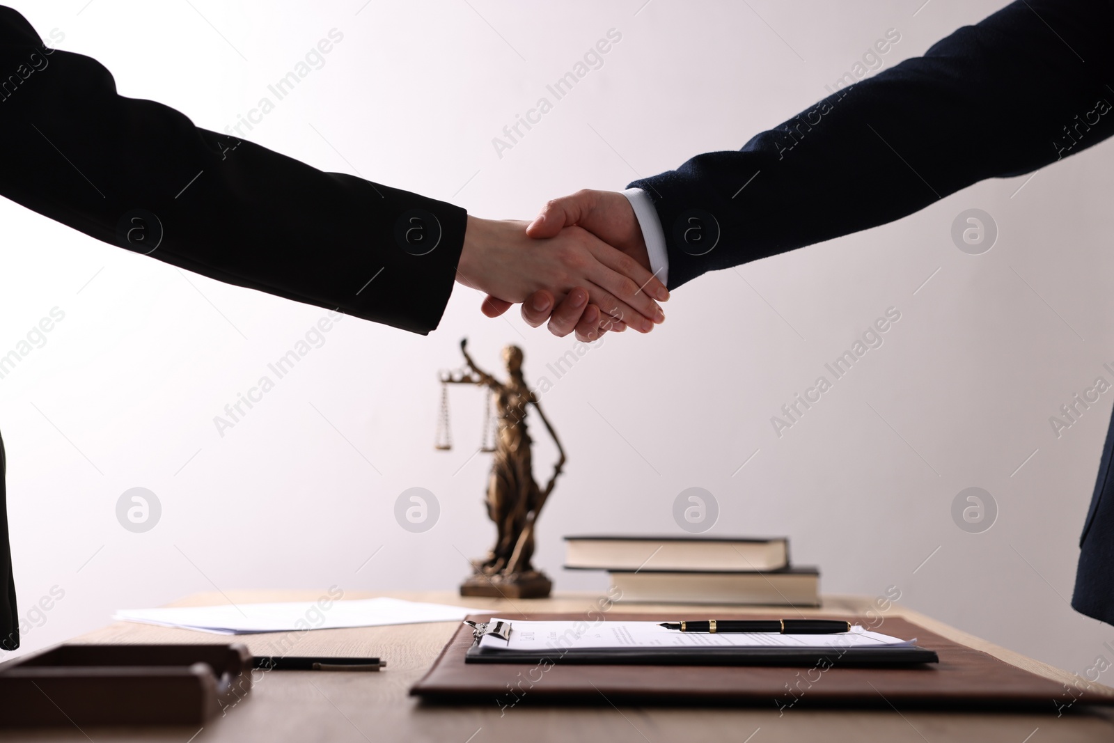 Photo of Notary shaking hands with client at wooden table in office, closeup