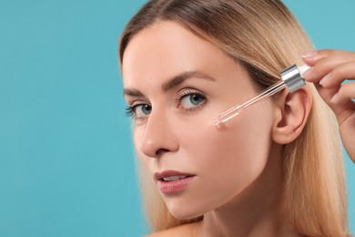 Beautiful woman applying cosmetic serum onto her face on light blue background, closeup. Space for text