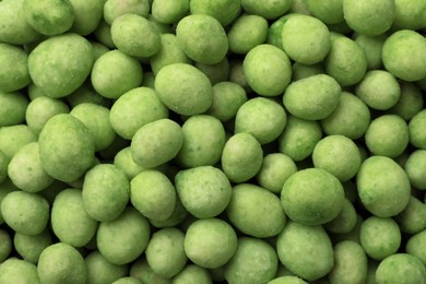 Tasty wasabi coated peanuts as background, top view