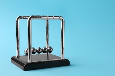 Photo of Newton's cradle on light blue background, space for text. Physics law of energy conservation
