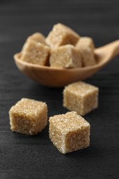 Photo of Spoon with brown sugar cubes on black wooden table, closeup