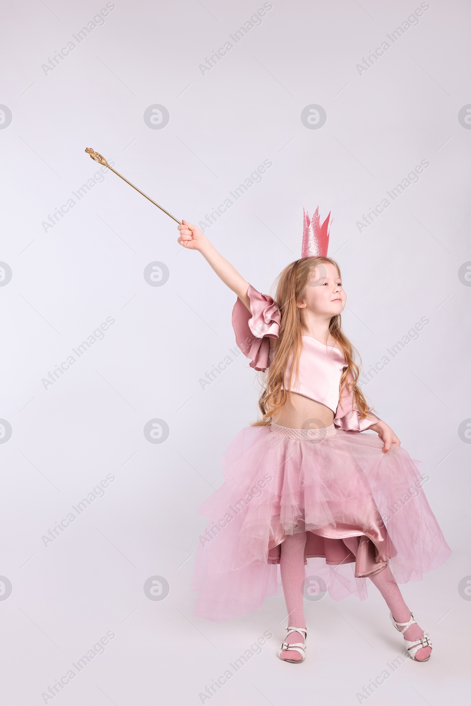 Photo of Cute girl in fairy dress with pink crown and magic wand on light grey background. Little princess